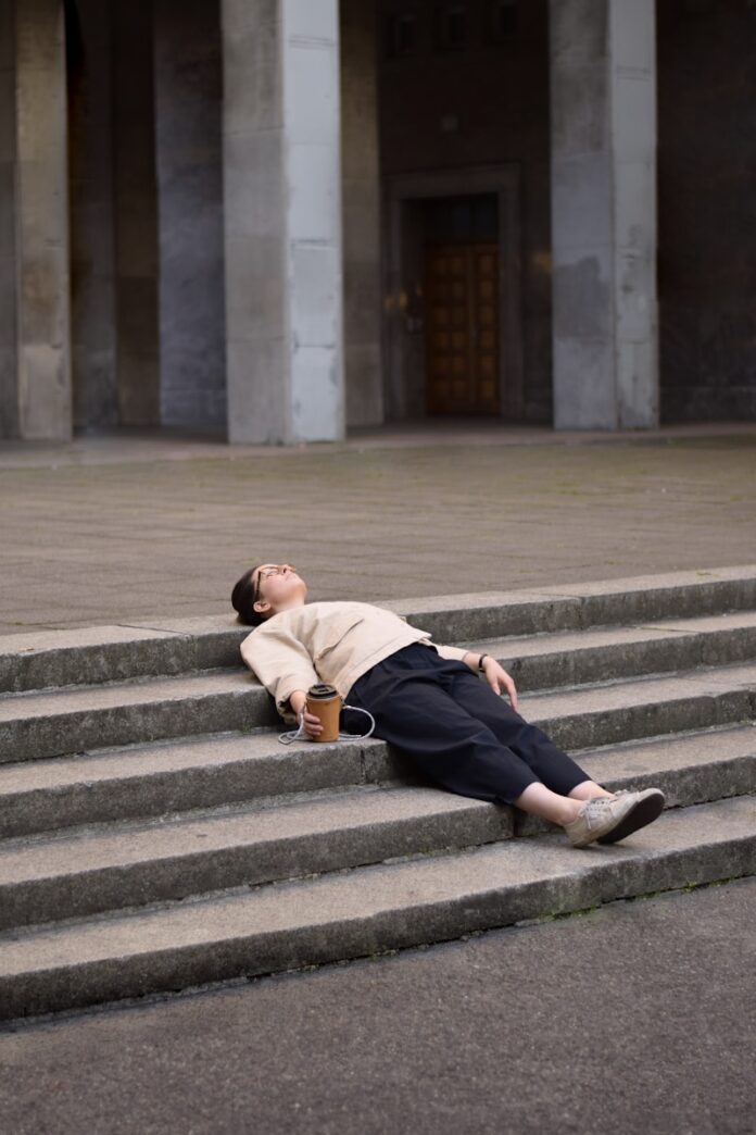 man in brown hoodie and black pants sitting on gray concrete stairs