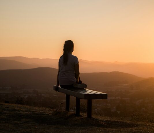스트레스를 마주하는 방식이 신경계와 면역에 스며드는 보이지 않는 영향 woman sitting on bench over viewing mountain